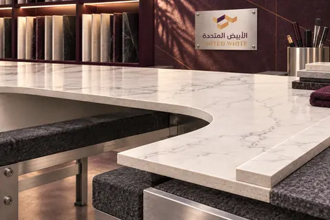 لوح سطح عمل من البورسلان الفاتح المعرّق يستند إلى طاولة عمل مبطنة، موضحاً حافة مستديرة لفتحة الحوض وشريط حواف مطابقاً.